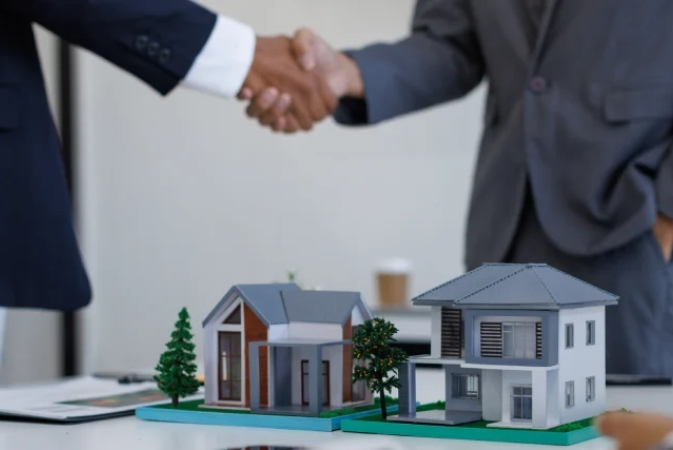 Two people shaking hands behind a model commercial buildings