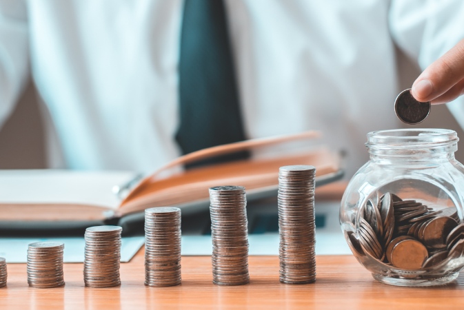 a person stacking coins next to a glass jar
